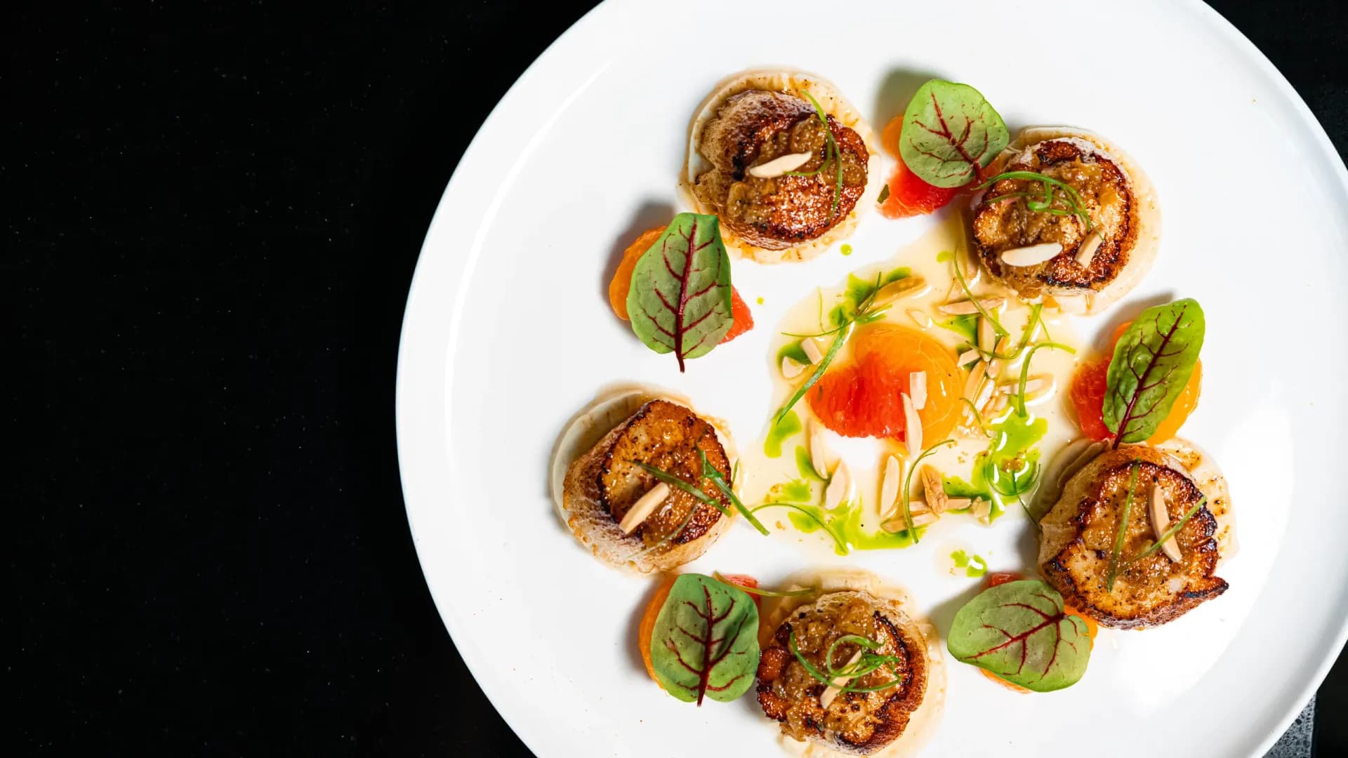 Six seared scallops arranged on a white plate with citrus segments, microgreens and herb oil at Ponte.