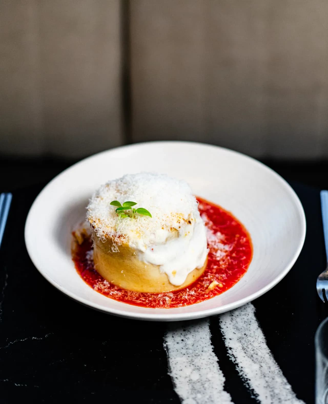 A golden baked pasta cake topped with shaved parmesan and basil, plated in red sauce at Olivia.