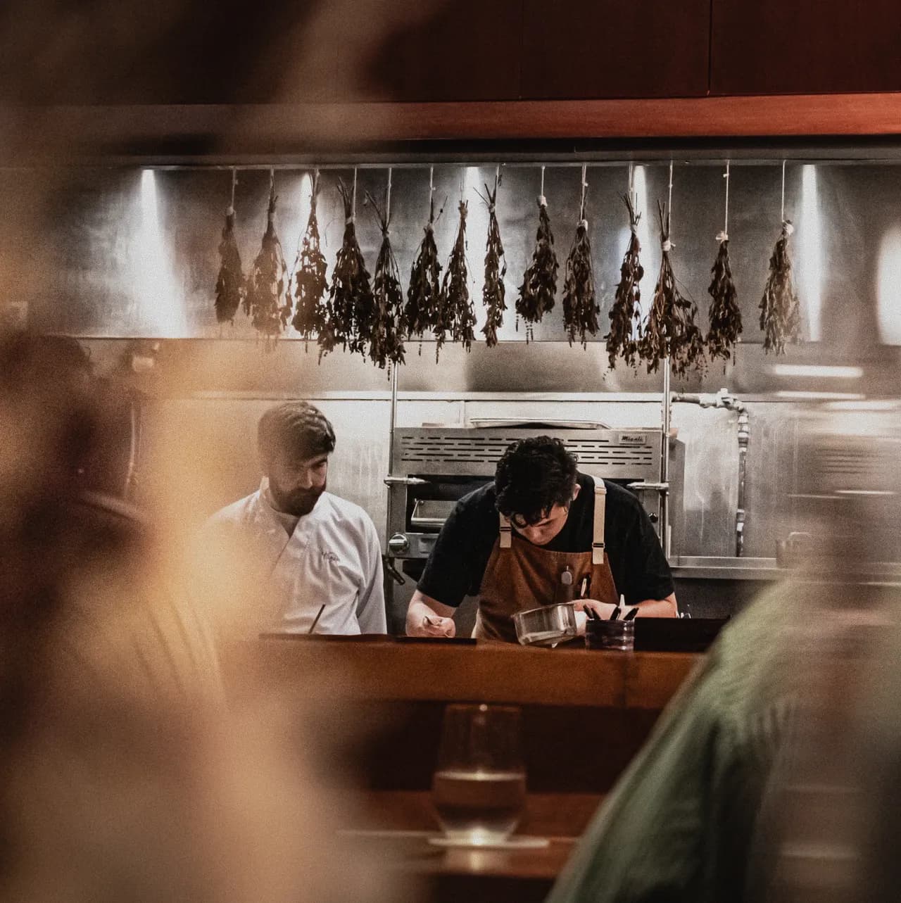 Chefs at work in Mei’s open kitchen, drying herbs hanging above the pass