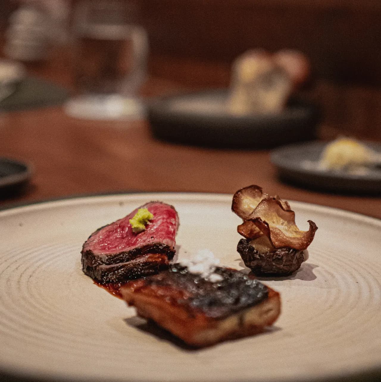Two seared pieces and a crisp mushroom chip on a stoneware plate at the counter