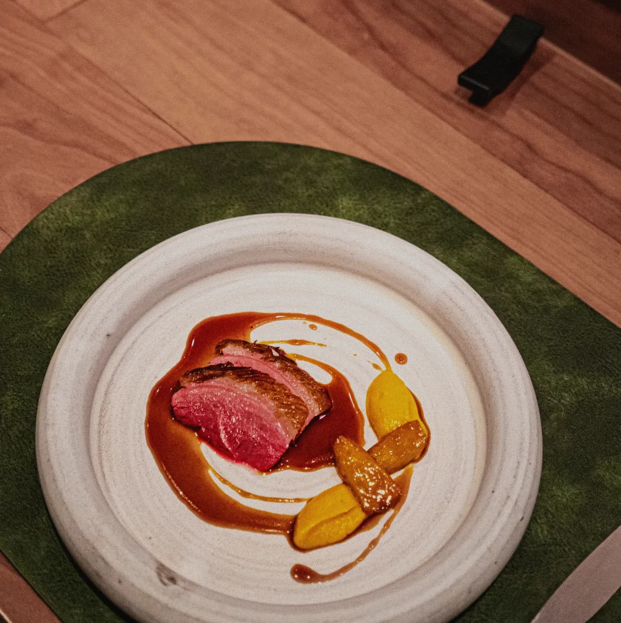 A sliced, pink-centred meat course with a glossy sauce and roasted fruit on a white ceramic plate
