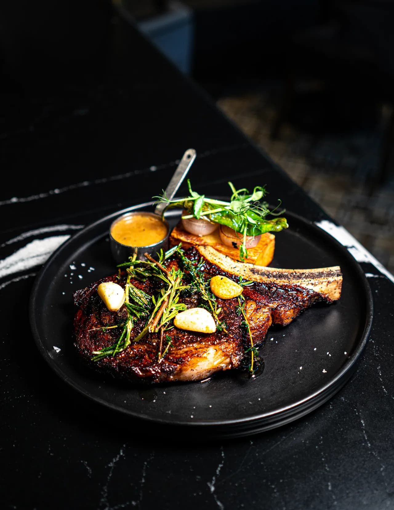 A bone-in steak with roasted garlic, herbs and sauce on the side at Olivia