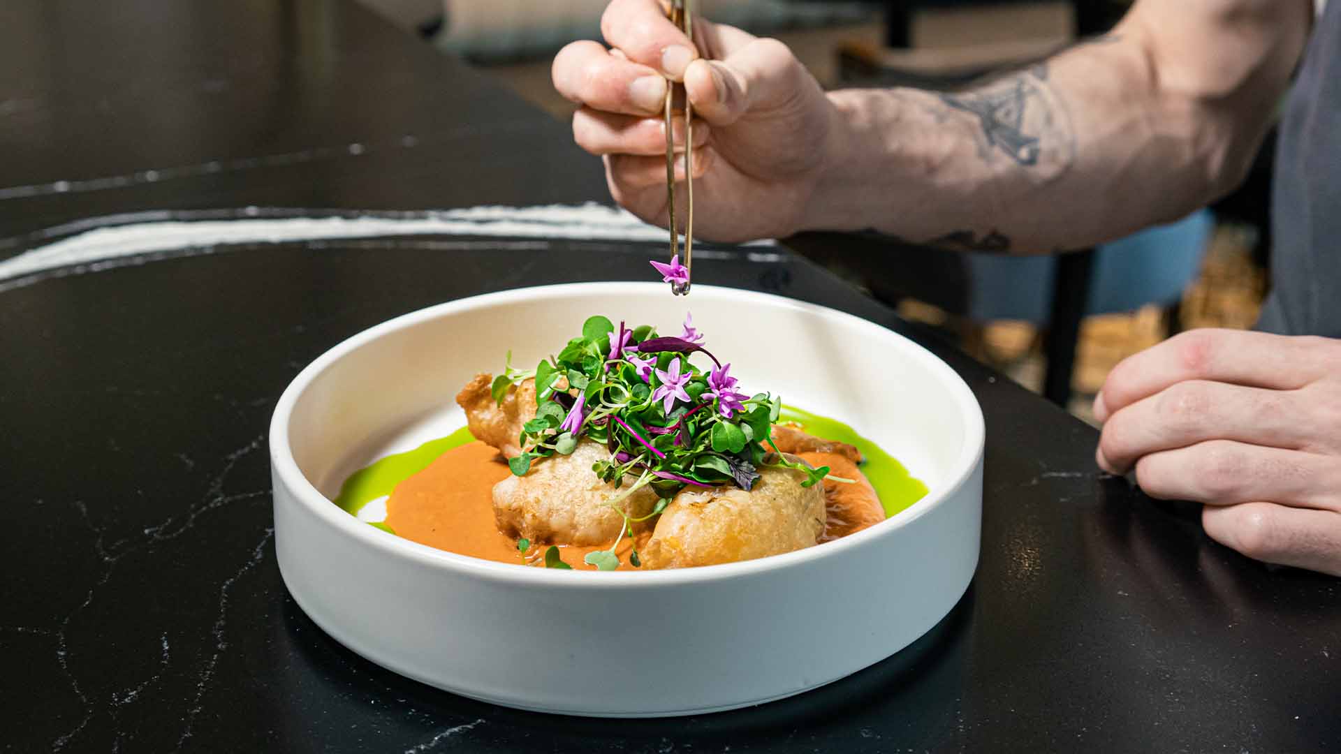 A chef finishing a plated dish with tweezers, adding a purple edible flower, at Ponte Modern American.
