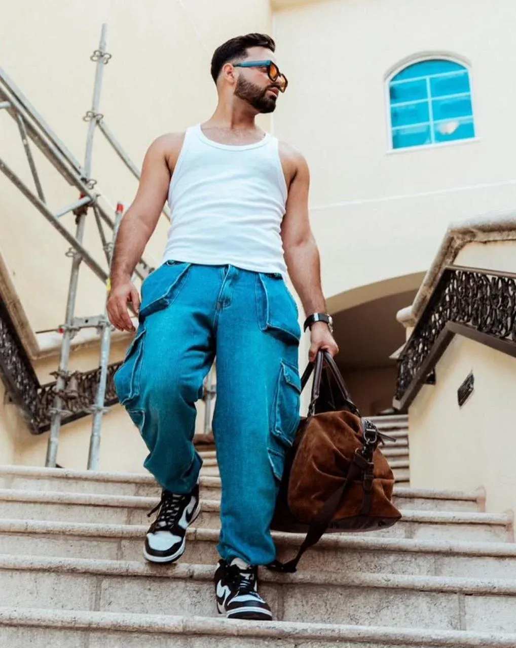 Jesus Andres Andrade walking down a staircase in sunglasses with a leather bag